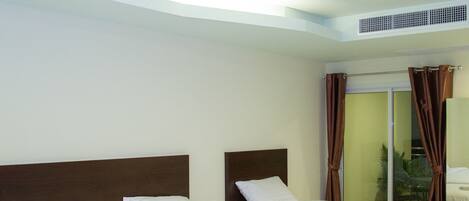 A hotel room with two beds, a large window with curtains, a ceiling fan, and a visible air conditioning unit.