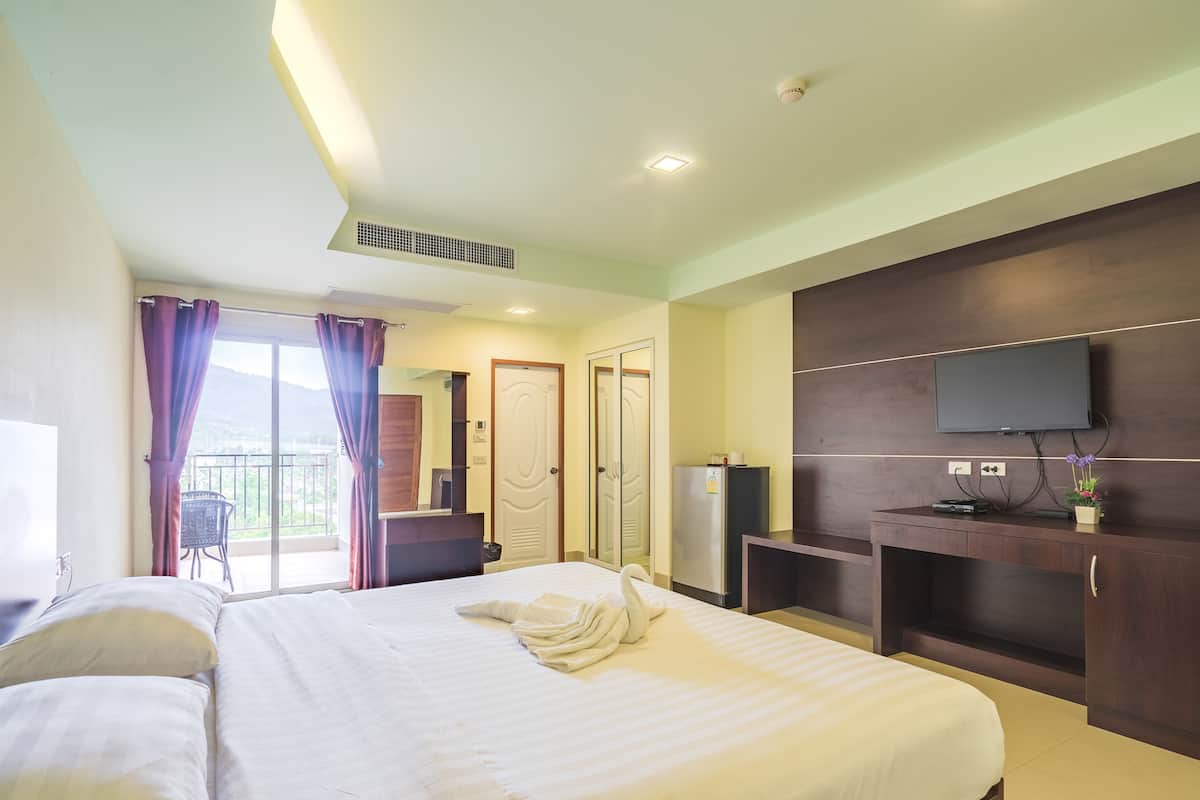 Habitación de hotel con una cama grande, un televisor de pantalla plana en la pared, un escritorio pequeño con una computadora y un balcón con una silla.