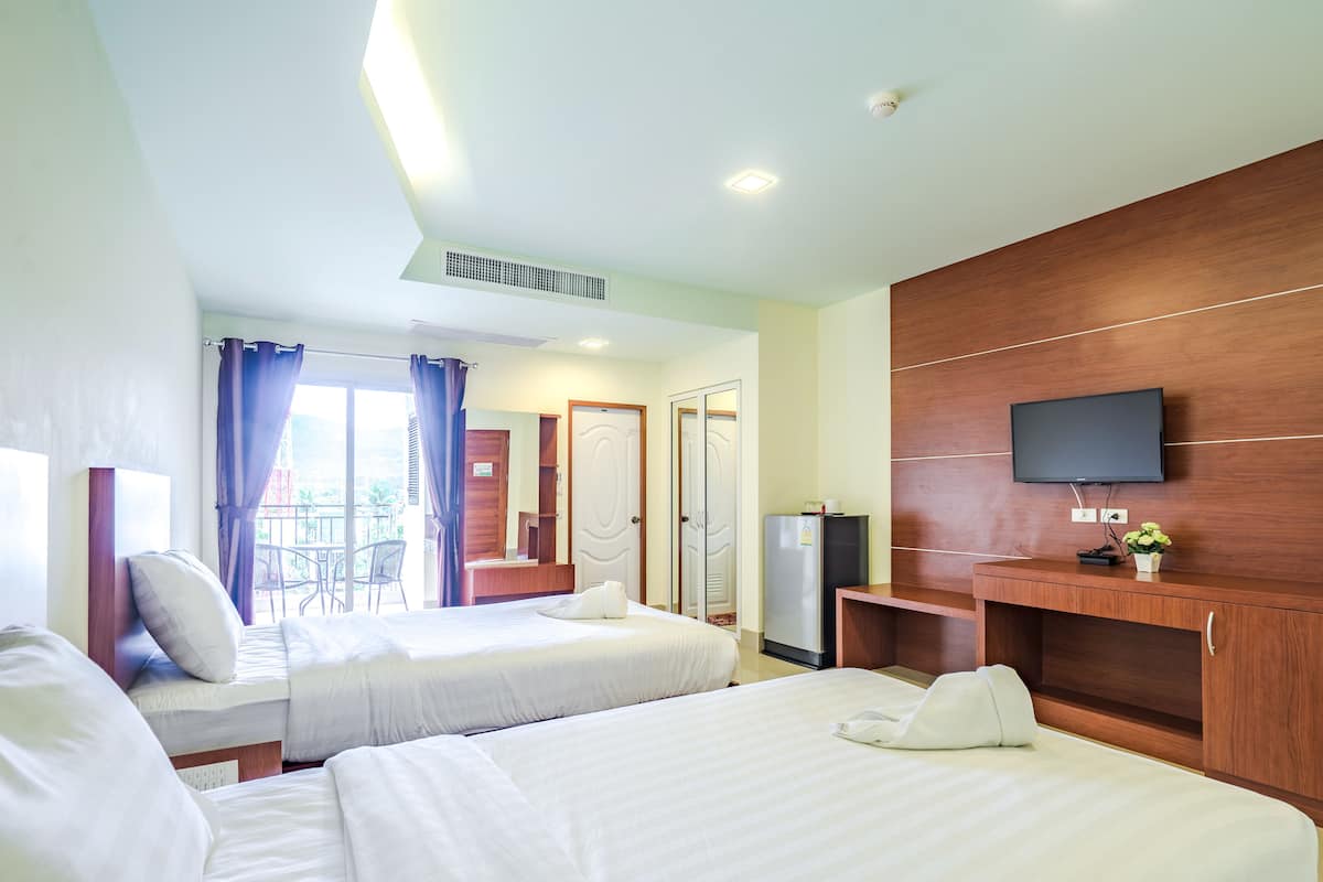 Habitación de hotel con dos camas, televisión, escritorio y balcón con una silla.