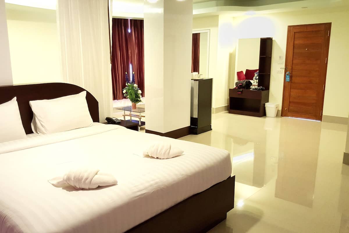 Una habitación de hotel con una cama grande, una mesita de noche con teléfono, un espejo, una planta pequeña y una puerta de madera.