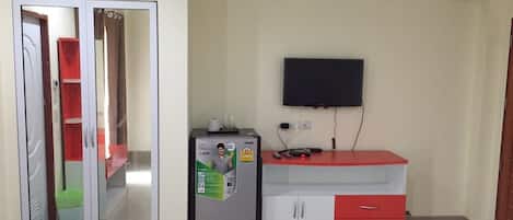 A compact room with a wardrobe, a small refrigerator, a TV mounted on the wall, and a red and white cabinet.