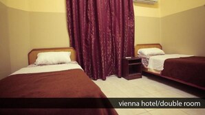 A double room with two beds, a wooden headboard, a nightstand, a window with curtains, and an air conditioning unit. - Hostel Vienna (Cairo)