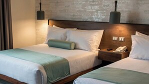 A hotel room with two beds, a nightstand with a phone, and a wall with a world map design.