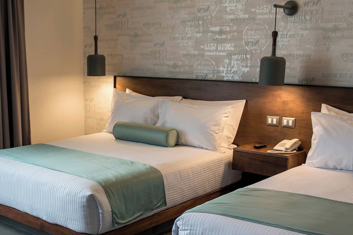 Habitación de hotel con dos camas, una mesita de noche con teléfono y una pared decorada con un mapa del mundo.