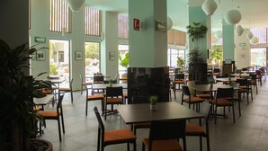 A spacious indoor dining area with multiple tables and chairs, large windows, and hanging spherical light fixtures.