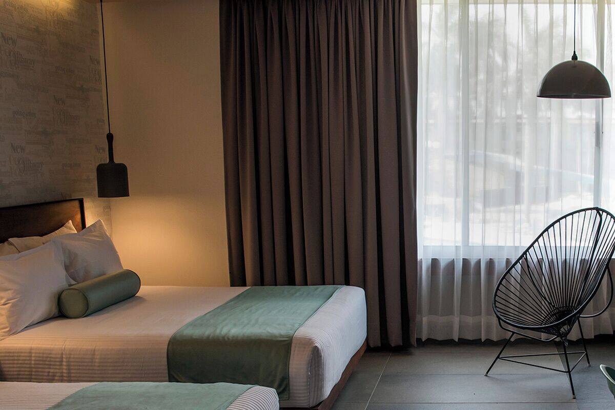Habitación de hotel con dos camas, una silla y un ventanal grande con cortinas.