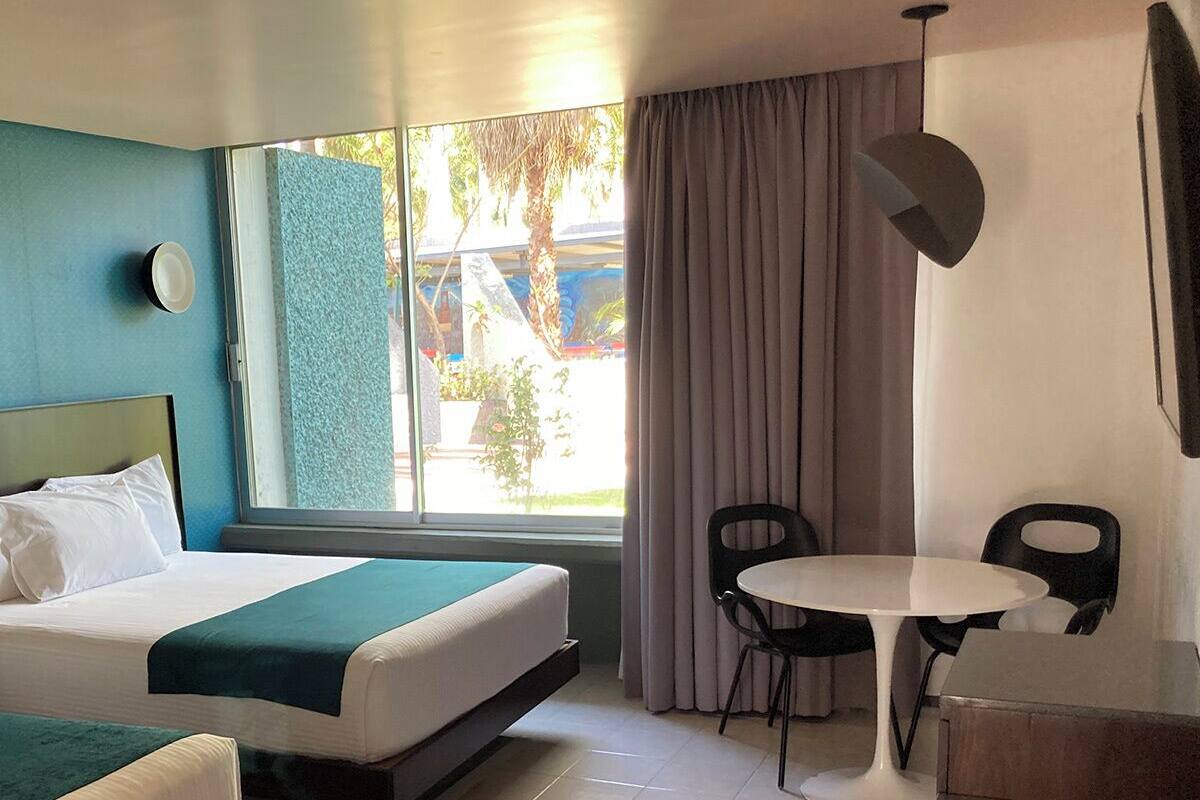 Habitación de hotel con cama, una pequeña mesa con dos sillas, un escritorio, una lámpara y una ventana con cortinas.