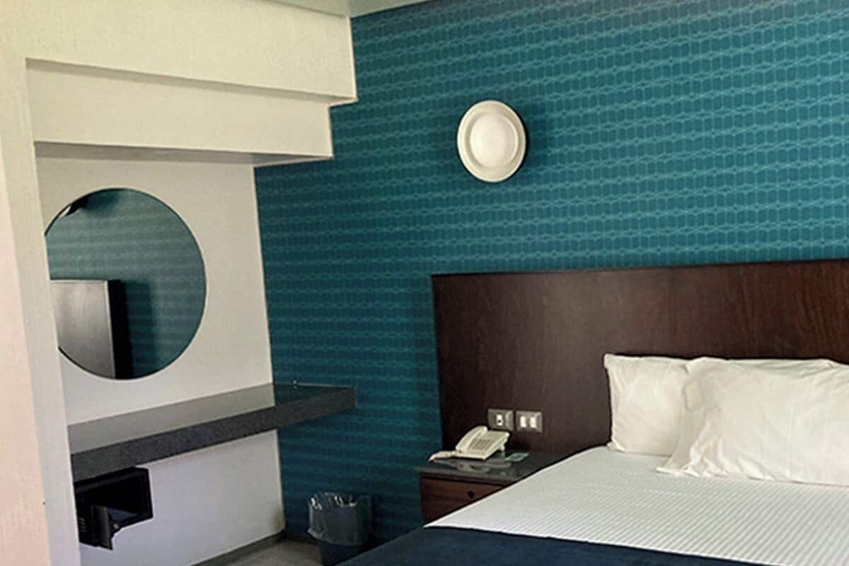 Una habitación de hotel moderna con una cama grande, una mesita de noche, un espejo y un teléfono en la pared.