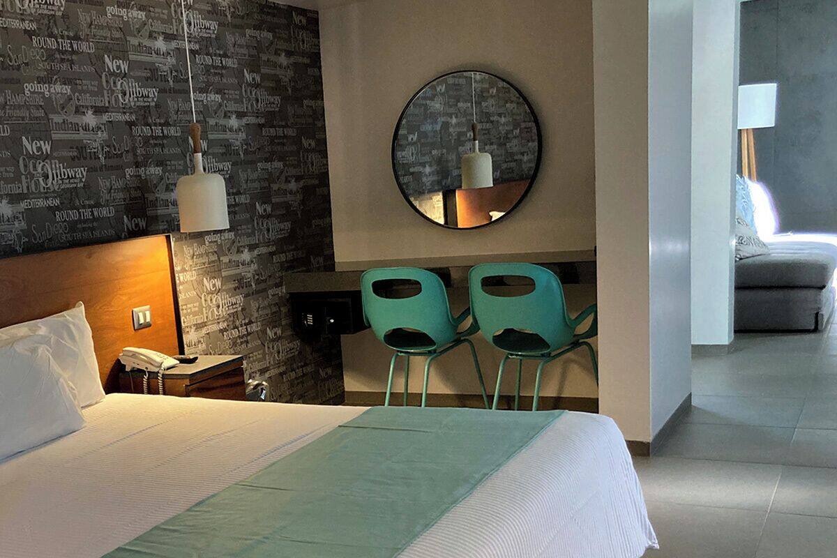 Habitación de hotel con una cama grande, un escritorio con dos sillas, un espejo redondo y una lámpara colgante.