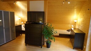 A wooden-paneled room with a TV on a dresser, a potted plant, and bedside lamps. - W&S Executive Apartments - Hallstatt II (Hallstatt)