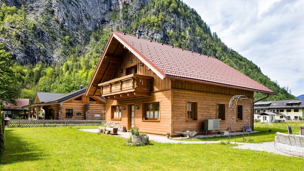 Un chalet in legno con tetto in tegole rosse, un balcone e vista su un paesaggio montano.