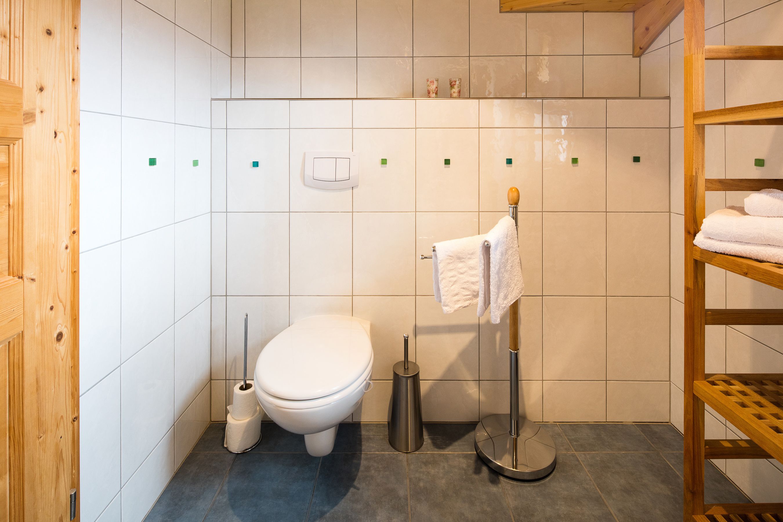 Une petite salle de bain propre, équipée d’un WC, d’un bidet, d’un porte-serviettes et d’une étagère en bois.
