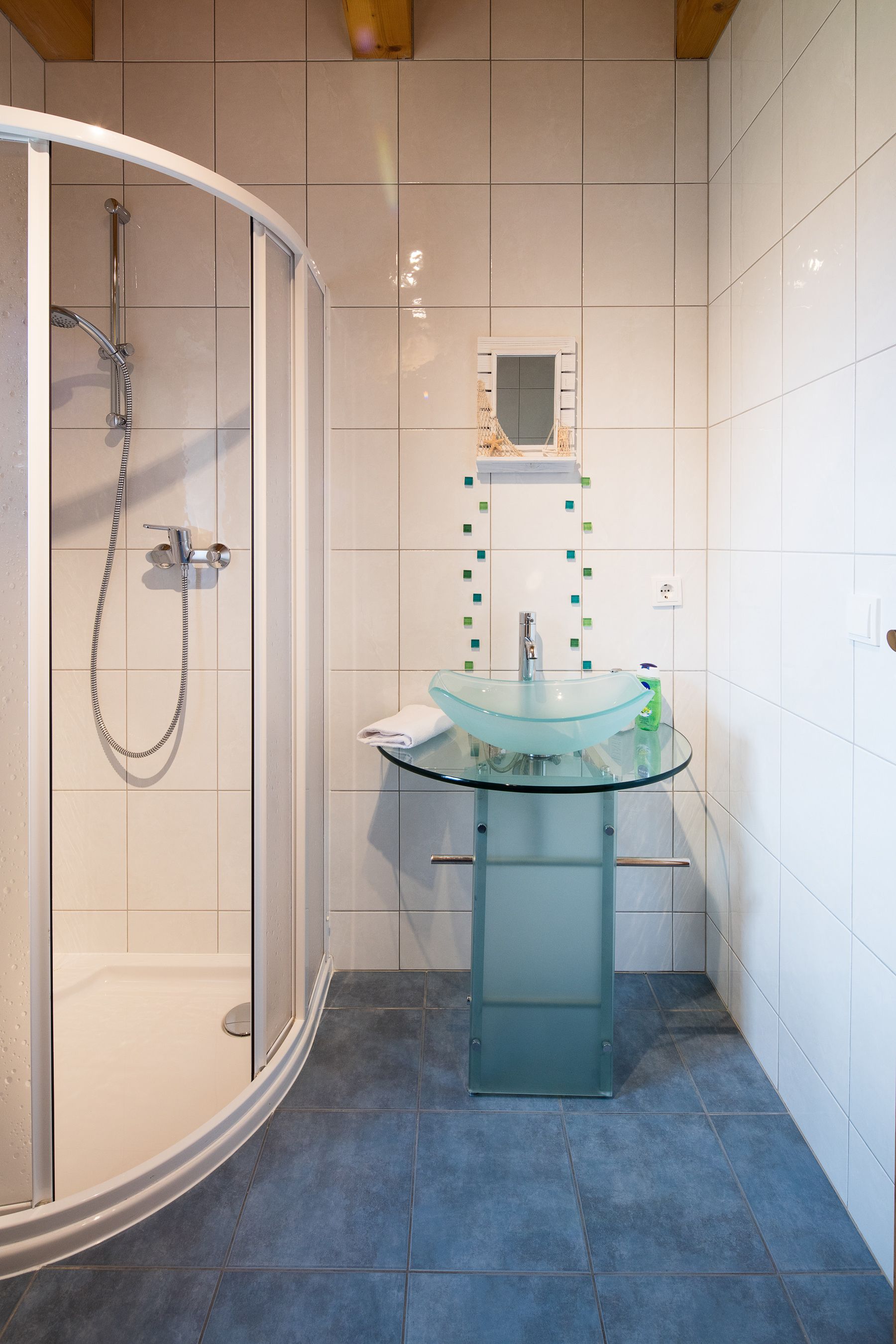 A modern bathroom with a glass-enclosed shower, a glass sink, and white tiled walls.