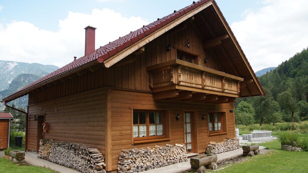 A wooden cabin with a sloped roof, a stone foundation, and a log stack outside. - W&S Executive Apartments - Hallstatt II (Hallstatt)