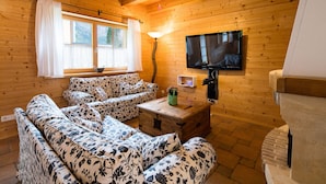 Un accogliente interno di una baita con pareti in legno, una poltrona, un televisore e un camino.