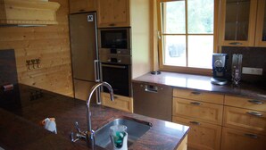 A kitchen with wooden cabinets, a stainless steel refrigerator, an oven, a microwave, a sink, and a window with a view of greenery. - W&S Executive Apartments - Hallstatt II (Hallstatt)