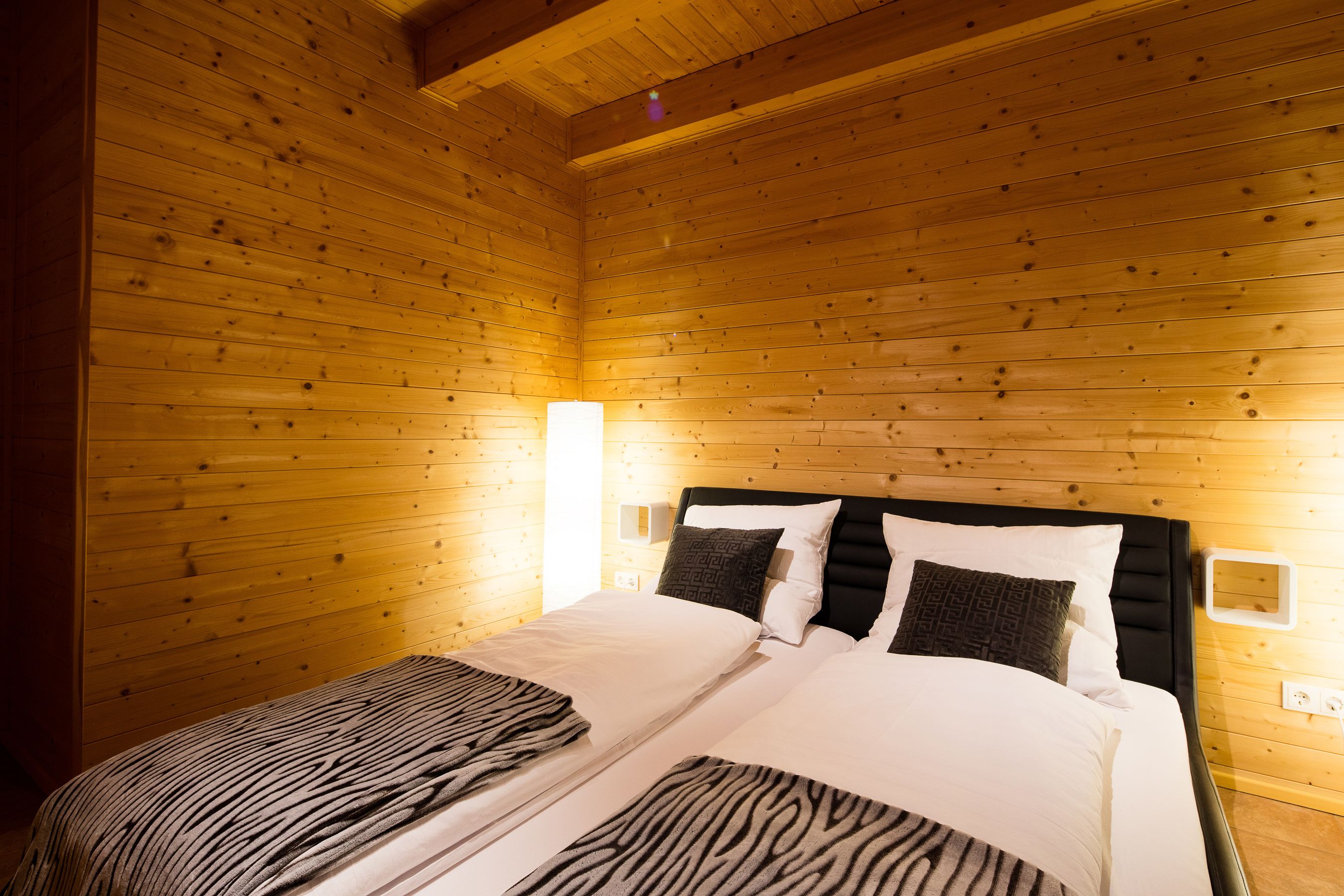 A wooden-paneled room with a bed, two bedside tables, and wall-mounted lamps.