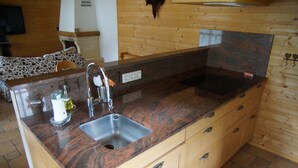 A kitchen with a granite countertop, stainless steel sink, wooden cabinets, and a stone backsplash. - W&S Executive Apartments - Hallstatt II (Hallstatt)