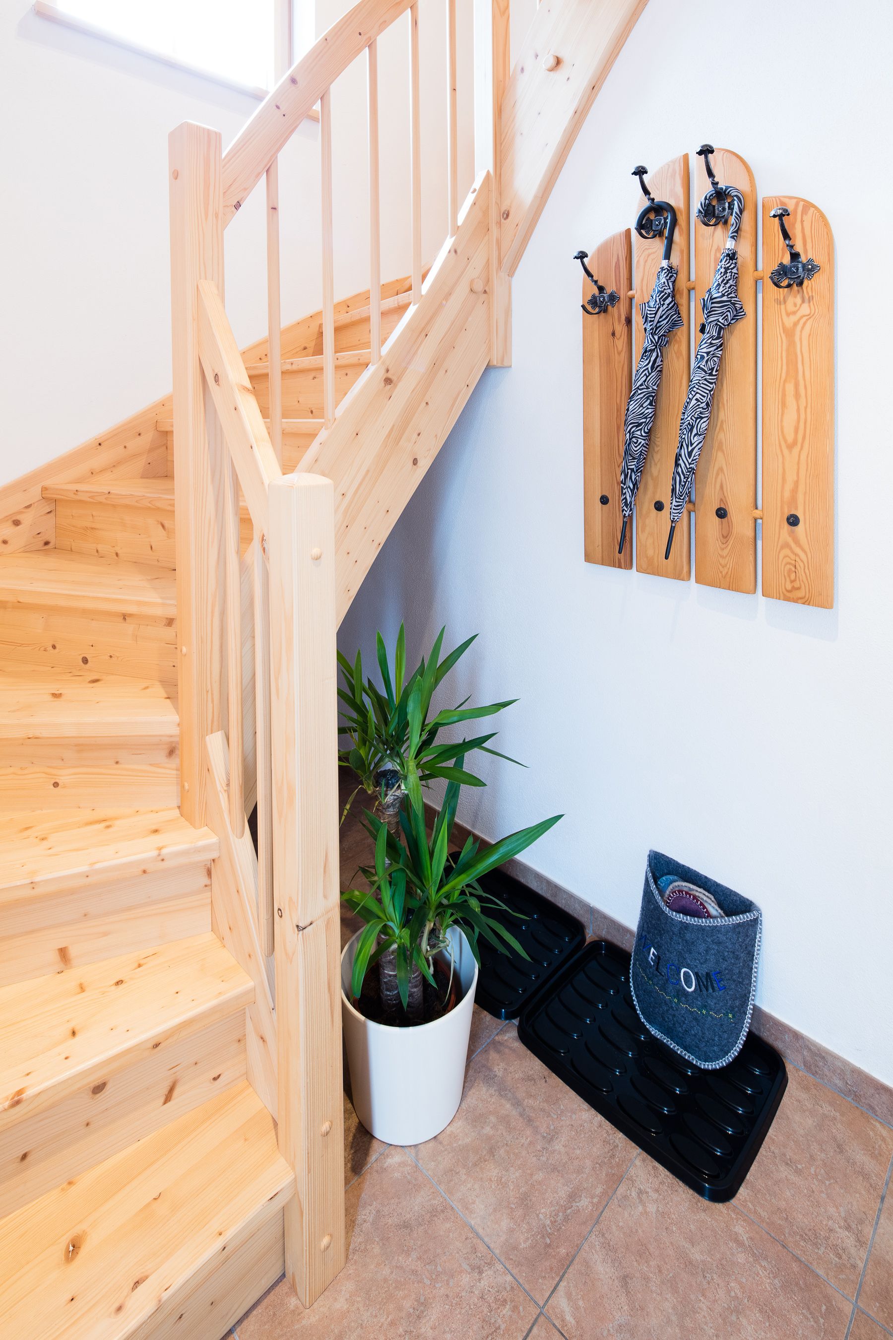 Una escalera de madera con una planta en maceta y un felpudo negro al final.