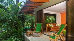 A modern outdoor seating area with wooden chairs and a sofa, surrounded by lush greenery and a thatched roof structure. - Olas Verdes Hotel (Nosara)