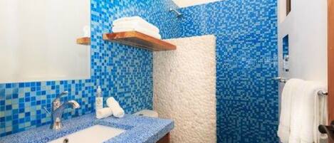 A bathroom with a blue mosaic tile wall, a white toilet, a sink with a blue countertop, and a shower area.