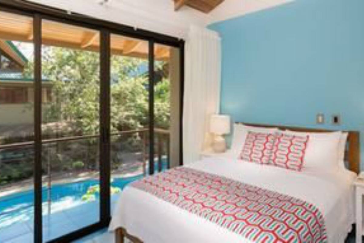 A bedroom with a large bed, a nightstand, and a view of a swimming pool.