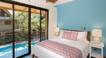 A bedroom with a large bed, a nightstand, and a view of a swimming pool.