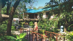 A wooden bridge with a metal railing leading to a building with a blue roof. - Olas Verdes Hotel (Nosara)