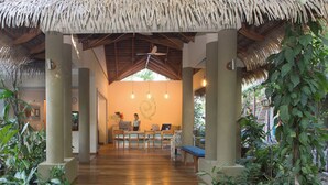 A reception area with a wooden desk, chairs, and a computer. There is a thatched roof structure and greenery around. - Olas Verdes Hotel (Nosara)