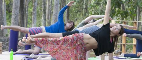 Menschen praktizieren Yoga auf Yogamatten im Freien, Bäume sind im Hintergrund zu sehen.