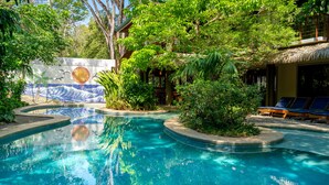 A swimming pool surrounded by lush greenery and a thatched-roof structure. - Olas Verdes Hotel (Nosara)