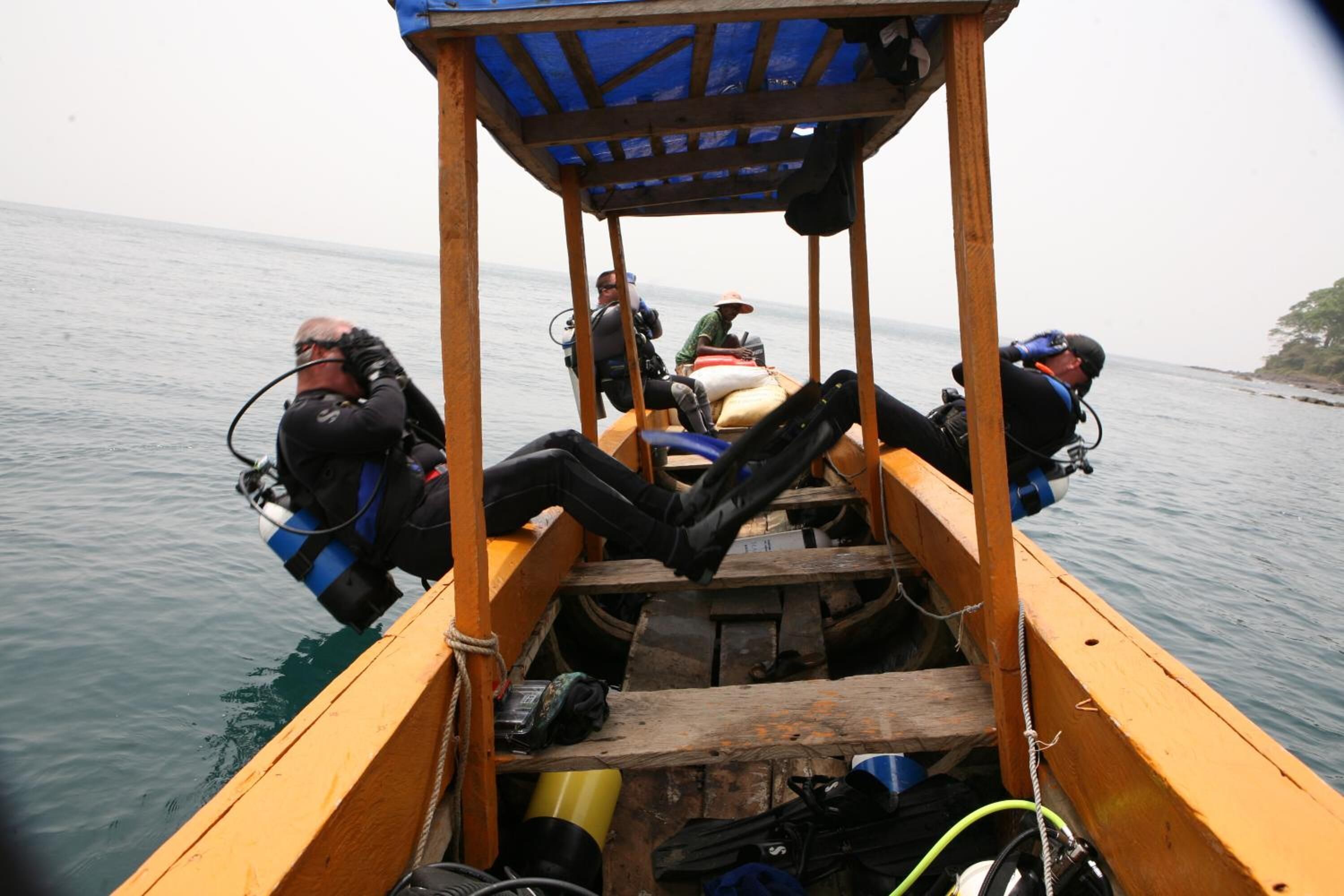 A wooden boat with four divers seated inside, equipped with scuba gear.