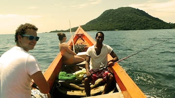 A small wooden boat with two people on it, one holding a fishing rod.