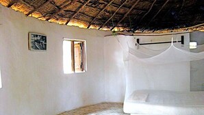Une pièce avec un lit, une petite fenêtre et un toit de chaume.