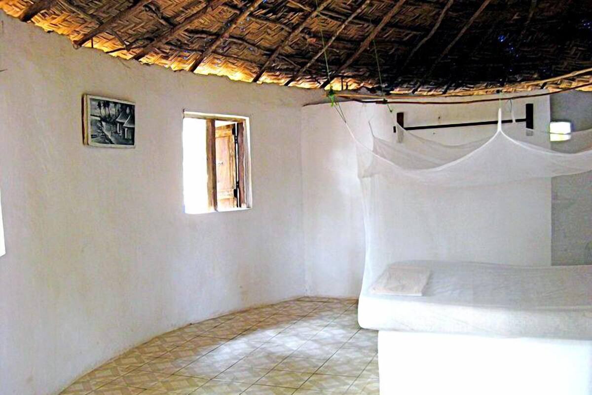 Una habitación con una cama, un ventanal pequeño y un techo de paja.
