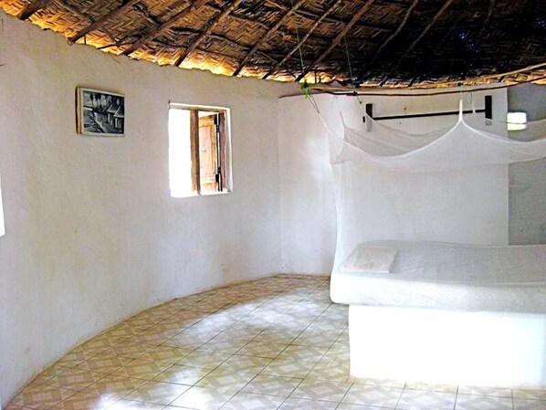 Una habitación con una cama, un ventanal pequeño y un techo de paja.