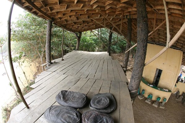 Una terraza de madera con techo de paja, rodeada de árboles.
