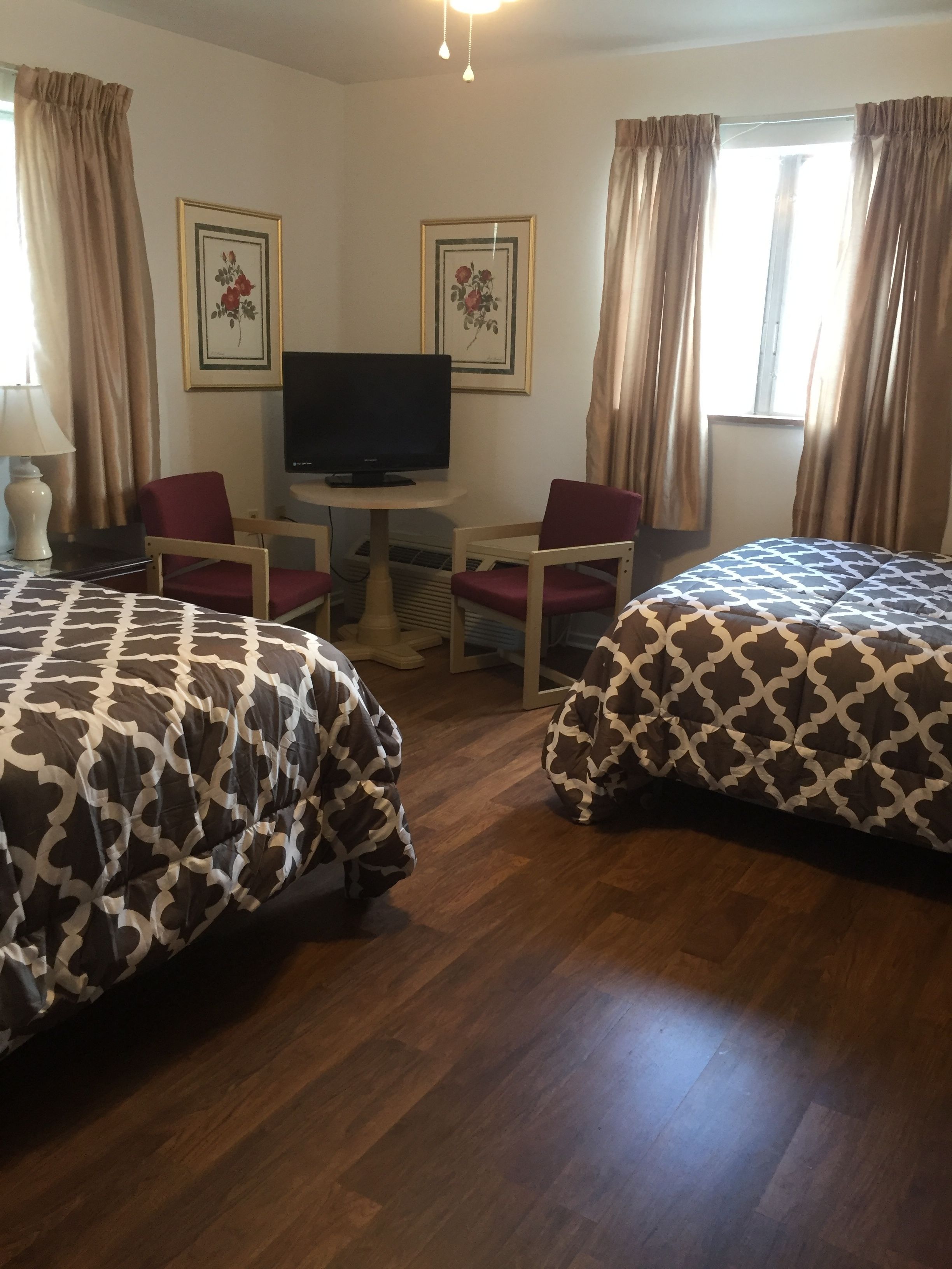 Una habitación de hotel con dos camas, un televisor sobre una mesita y dos sillas.