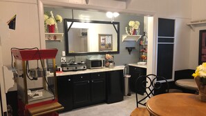 A compact kitchen with a microwave, stove, and sink. There is a dining area with a wooden table and chairs. - The Baxa Inn (Buckhannon)