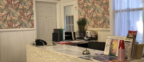 A reception desk with a patterned wallpaper, a chandelier, and a window with sheer curtains.