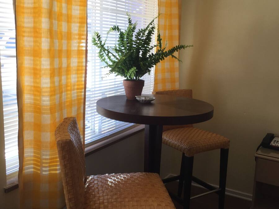 Un comedor con una mesa redonda, dos sillas de mimbre, una planta en maceta y una ventana con persianas.