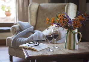 A cozy reading nook with a chair, a blanket, a book, two wine glasses, and a vase with flowers.