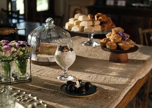 A buffet table with various pastries, a glass dessert bowl, and a floral arrangement.