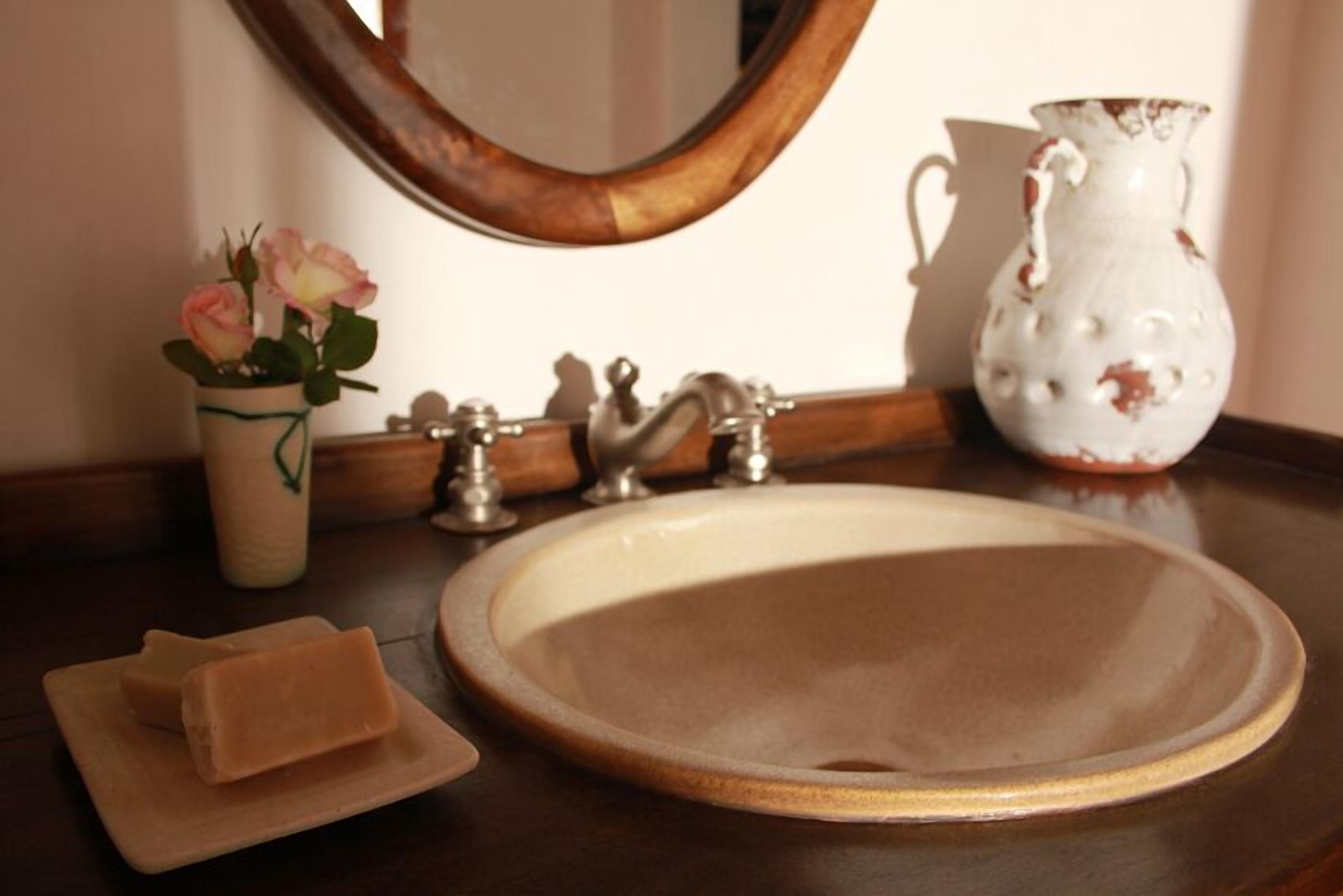Un lavabo dans la salle de bain, avec un miroir, un vase de fleurs et une carafe.
