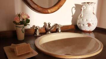 Un lavabo dans la salle de bain, avec un miroir, un vase de fleurs et une carafe.