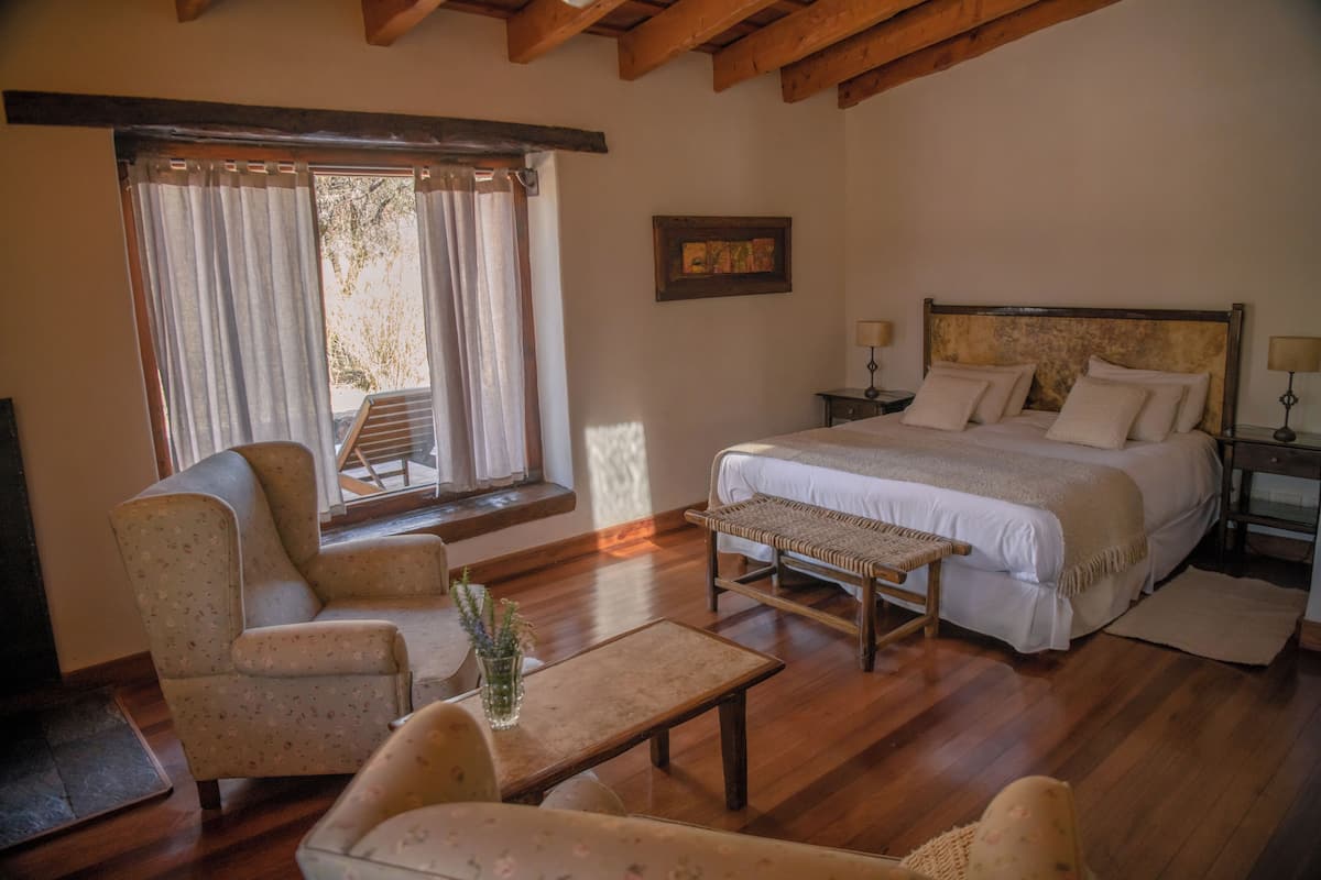 A bedroom with a bed, two bedside tables, a chair, a small table, and a window with curtains.