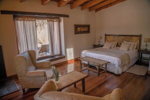 A bedroom with a bed, two bedside tables, a chair, a small table, and a window with curtains.