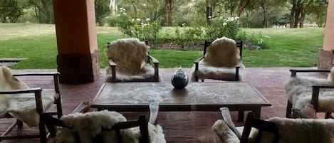 Un patio al aire libre con cuatro sillas y una mesa, rodeado de un suelo de ladrillo y pilares grandes.