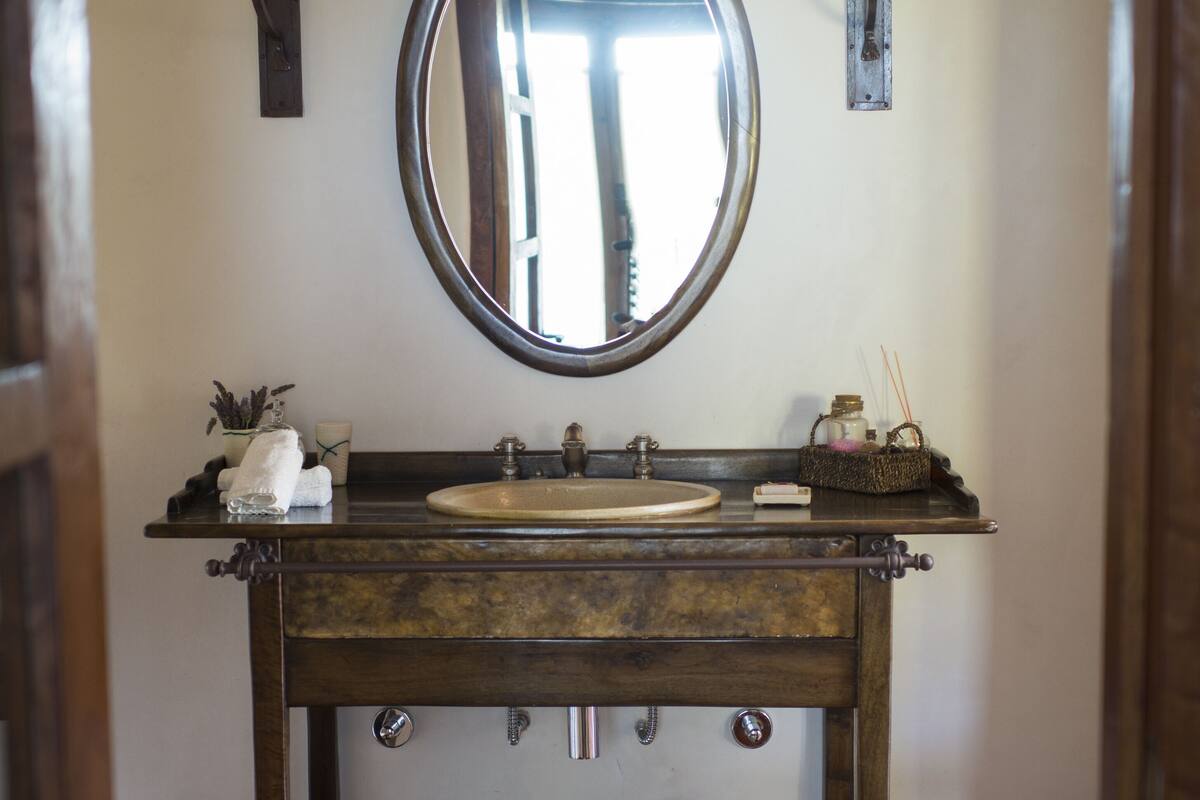 A bathroom with a wooden vanity, a round mirror, two wall-mounted lamps, and a sink.