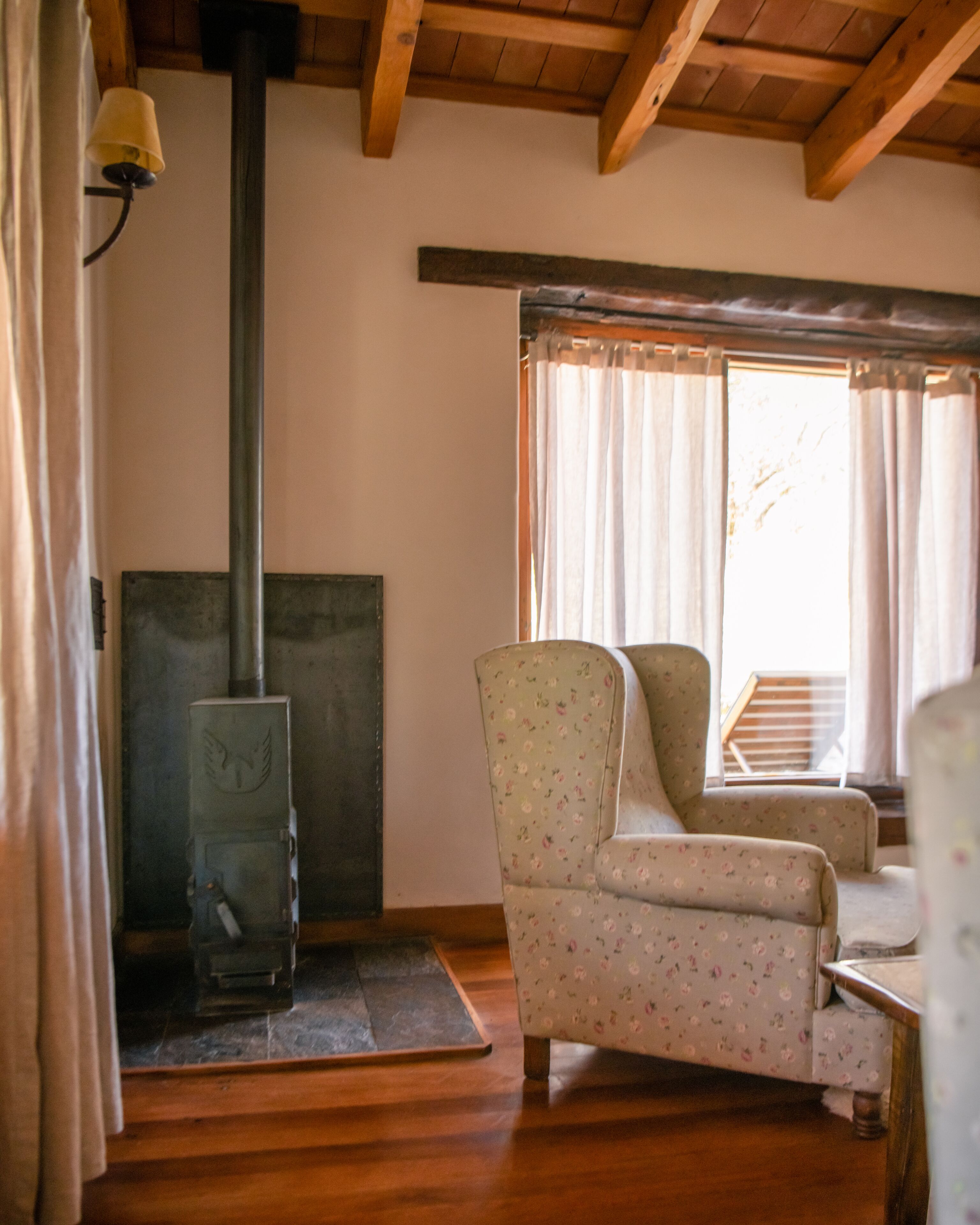 Una habitación acogedora con chimenea, vigas de madera y sillones estampados con motivos florales.